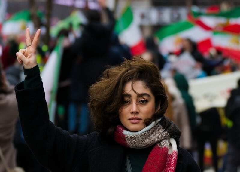 Young Woman in Coat and Scarf Showing a Peace Sign at a Protest