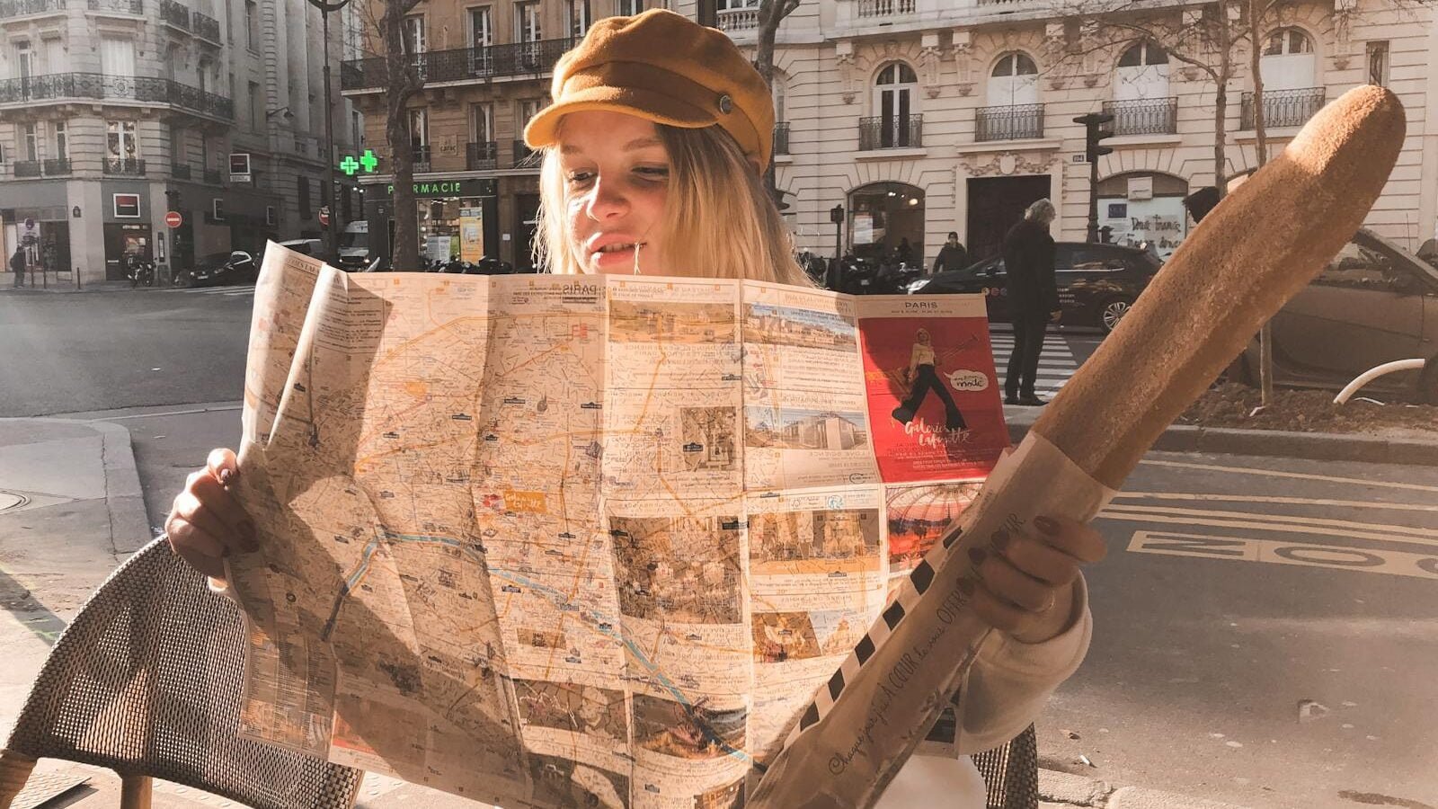 Photo of Sitting Woman Holding Baguette While Reading a Map