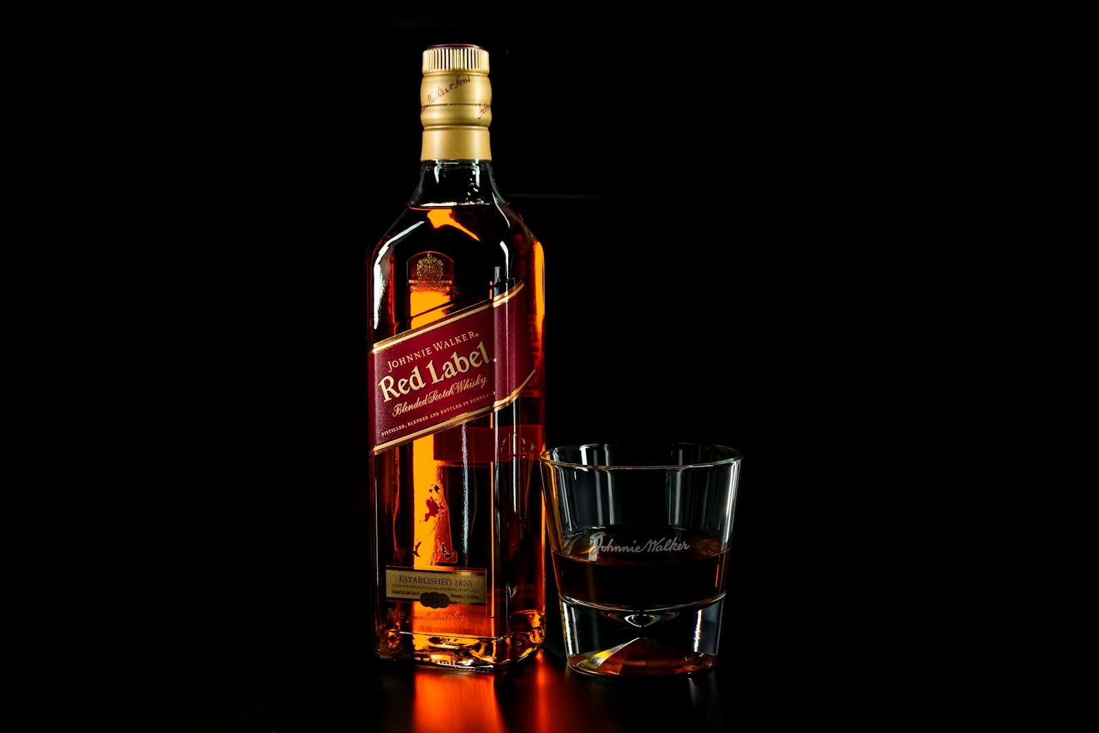 Shallow Focus Photo of Red Label Liquor Bottle Beside Drinking Glass