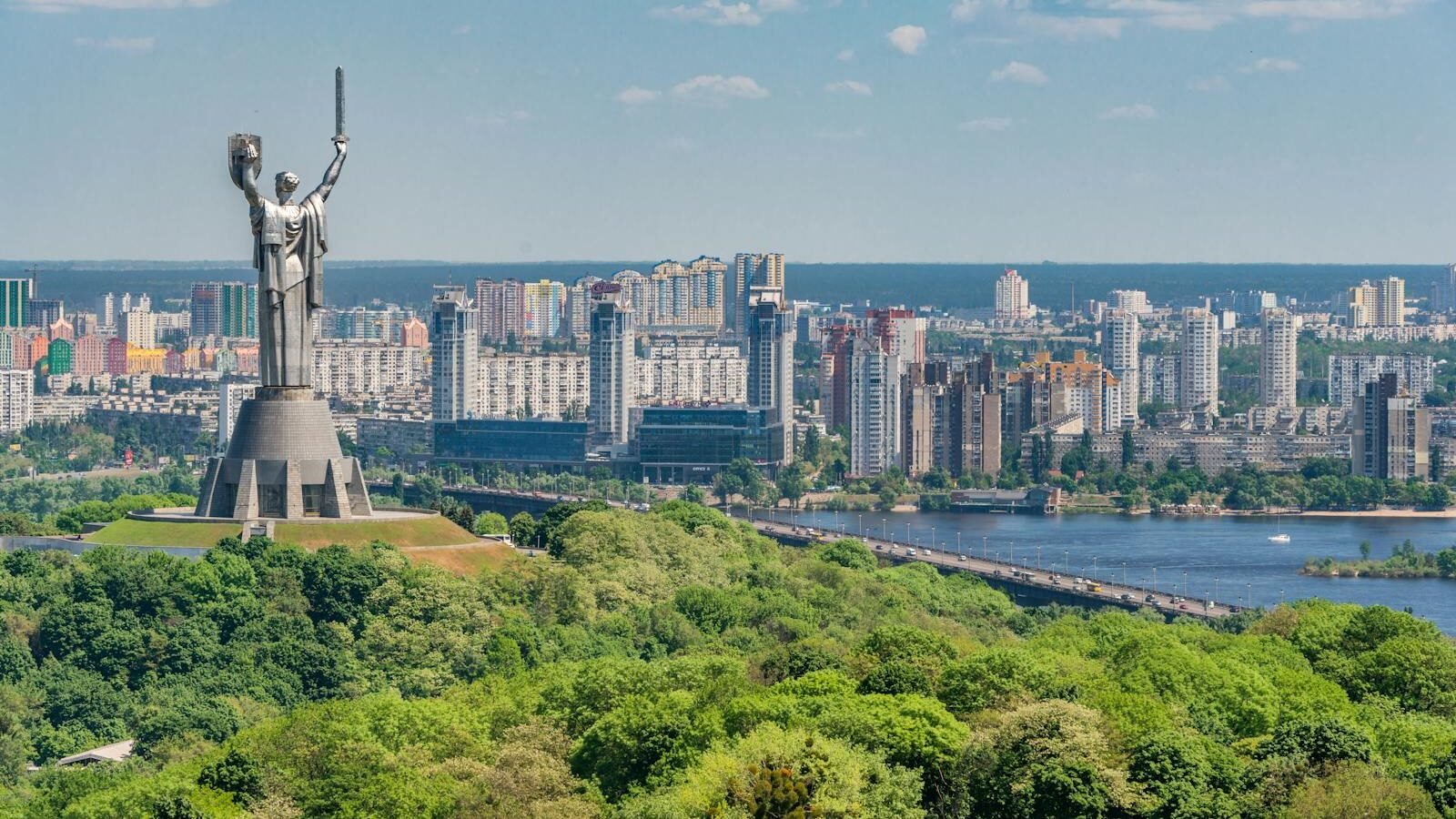 Motherland Monument among green trees on embankment in Kiev