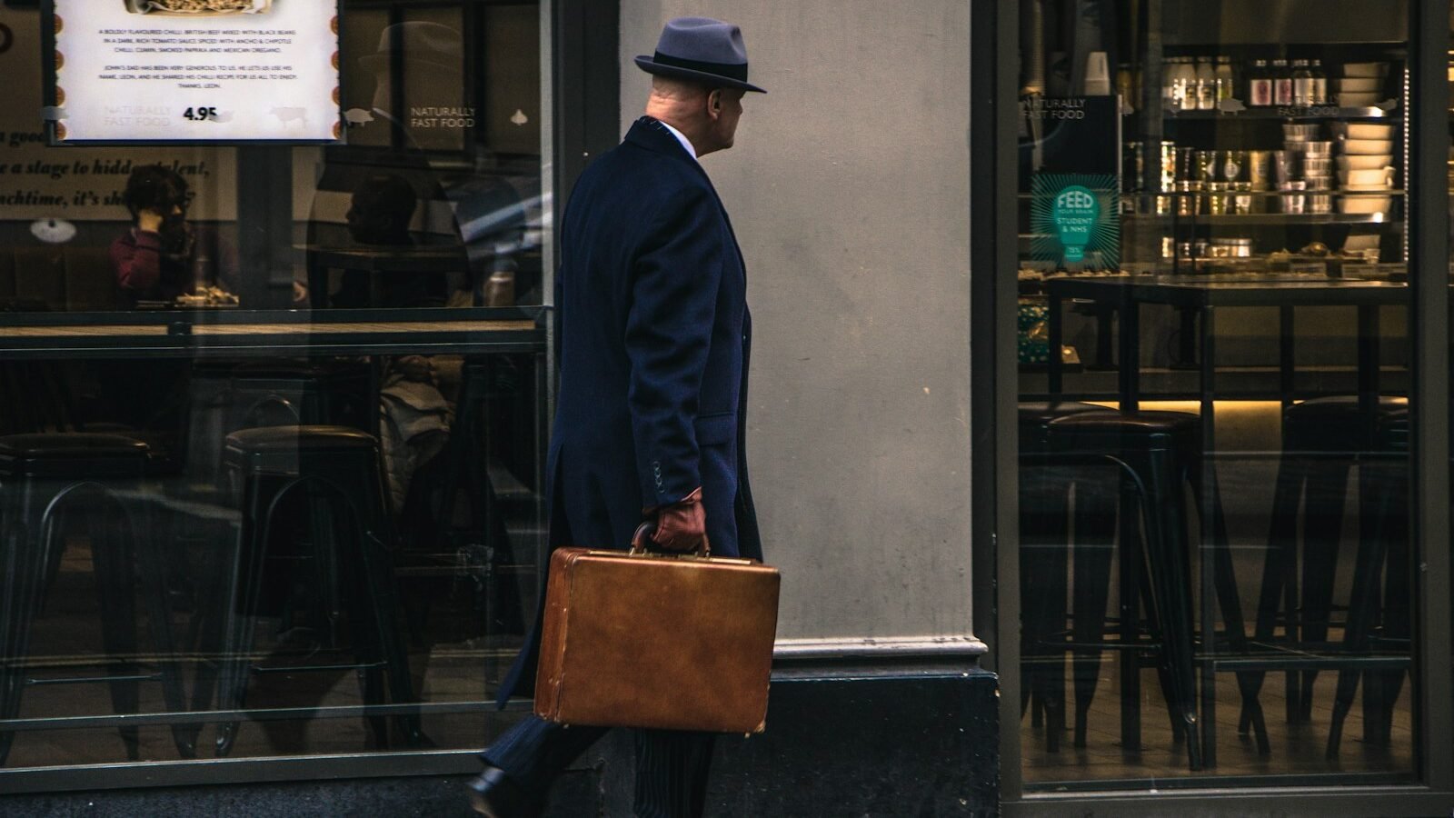 man in black suit jacket and blue hat standing in front of store